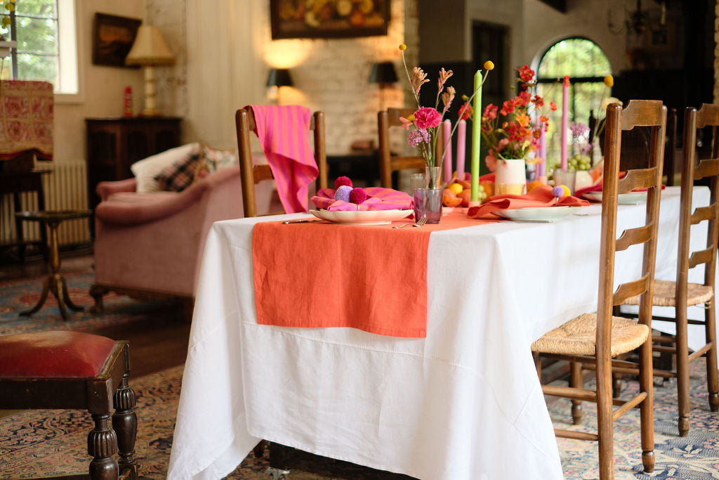 Table setting with white table cloth, orange table runner and bright pink stripy napkins