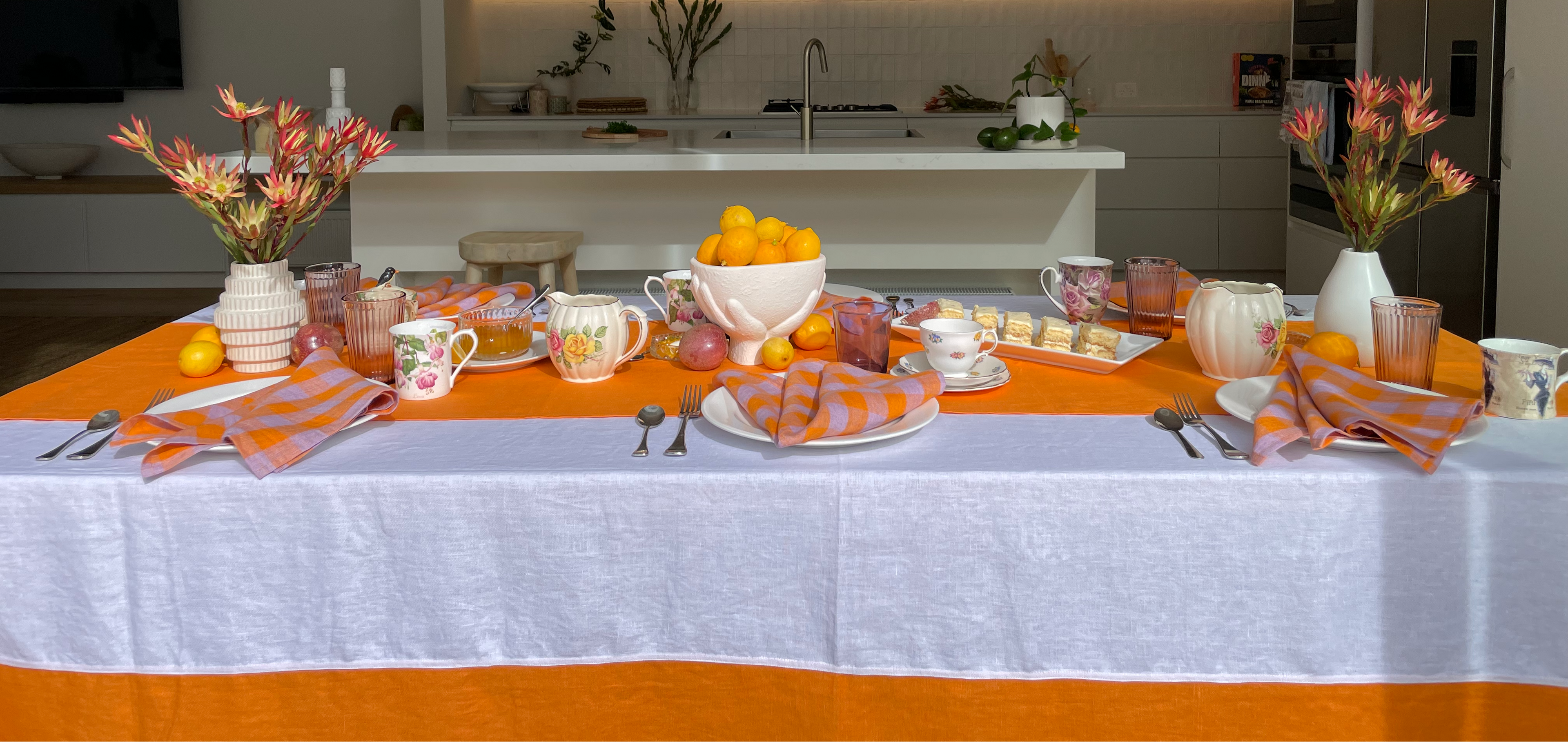 Dining table set with orange tablecloth, white tablecloth, and decorative items in a modern kitchen.